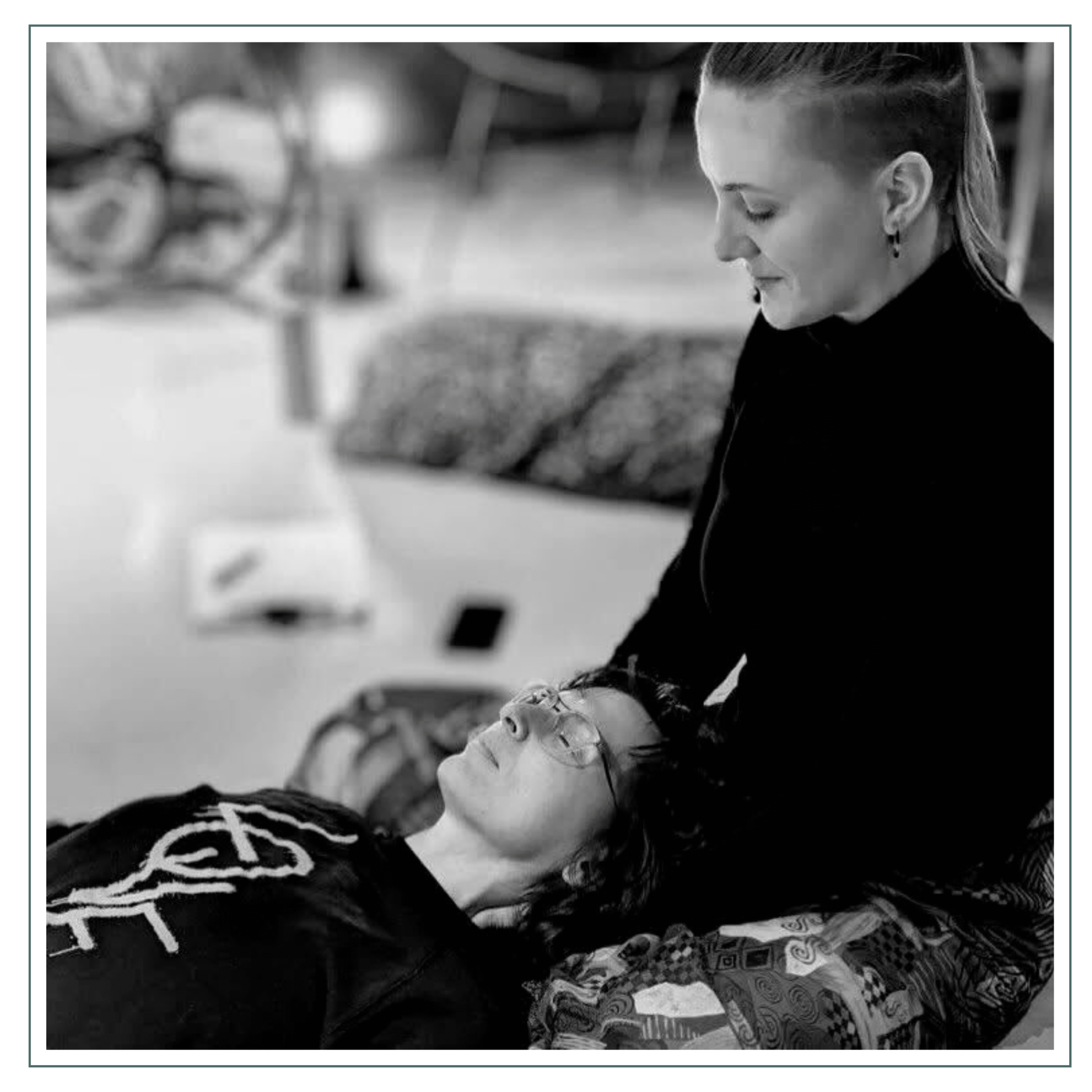 A person is lying down while receiving a bodywork or energy healing session, with another person sitting nearby, possibly providing the treatment. The setting looks relaxed and calm.