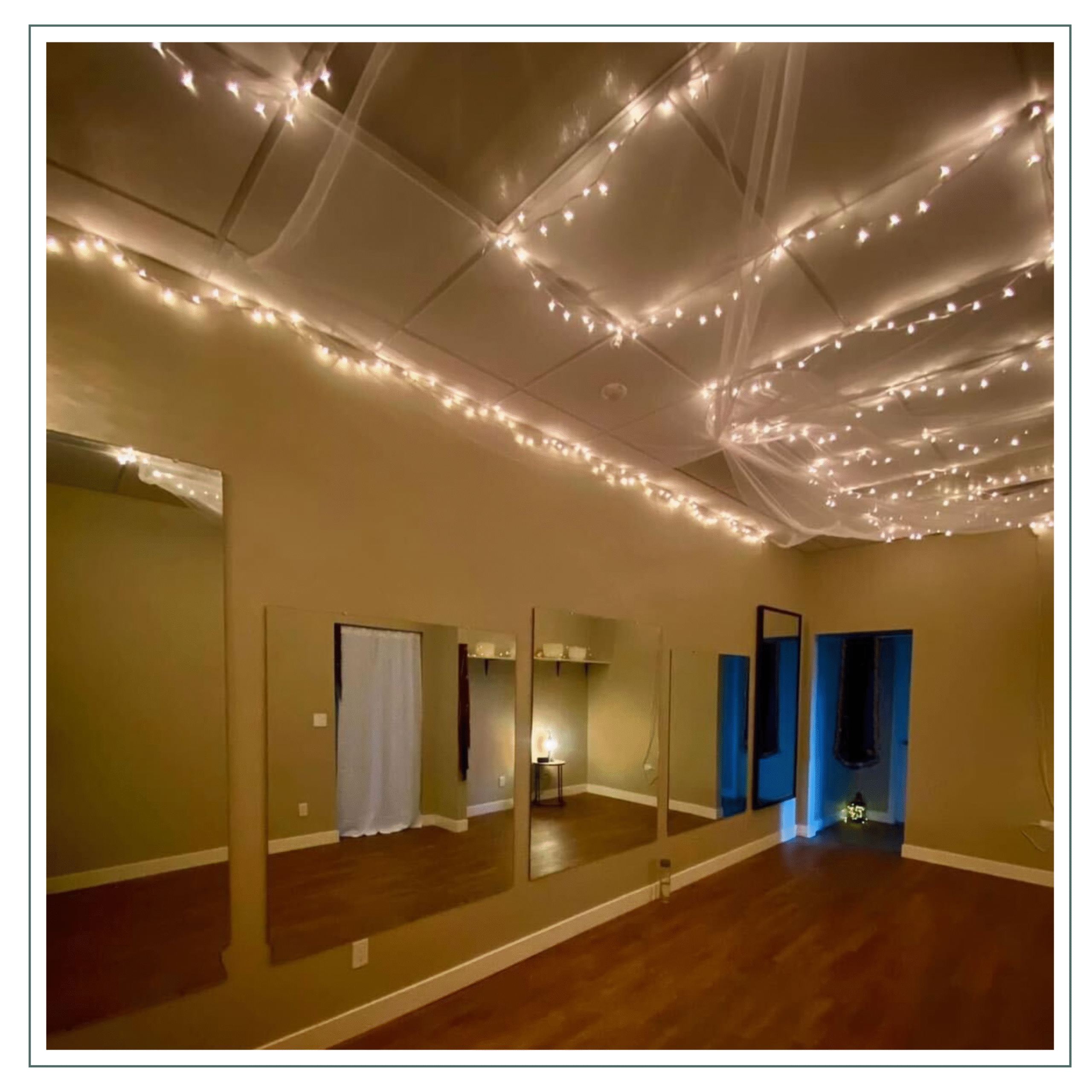 A peaceful and cozy room with soft lighting from string lights on the ceiling. The space has mirrors on one wall and a warm, inviting atmosphere, possibly used for wellness or relaxation activities.
