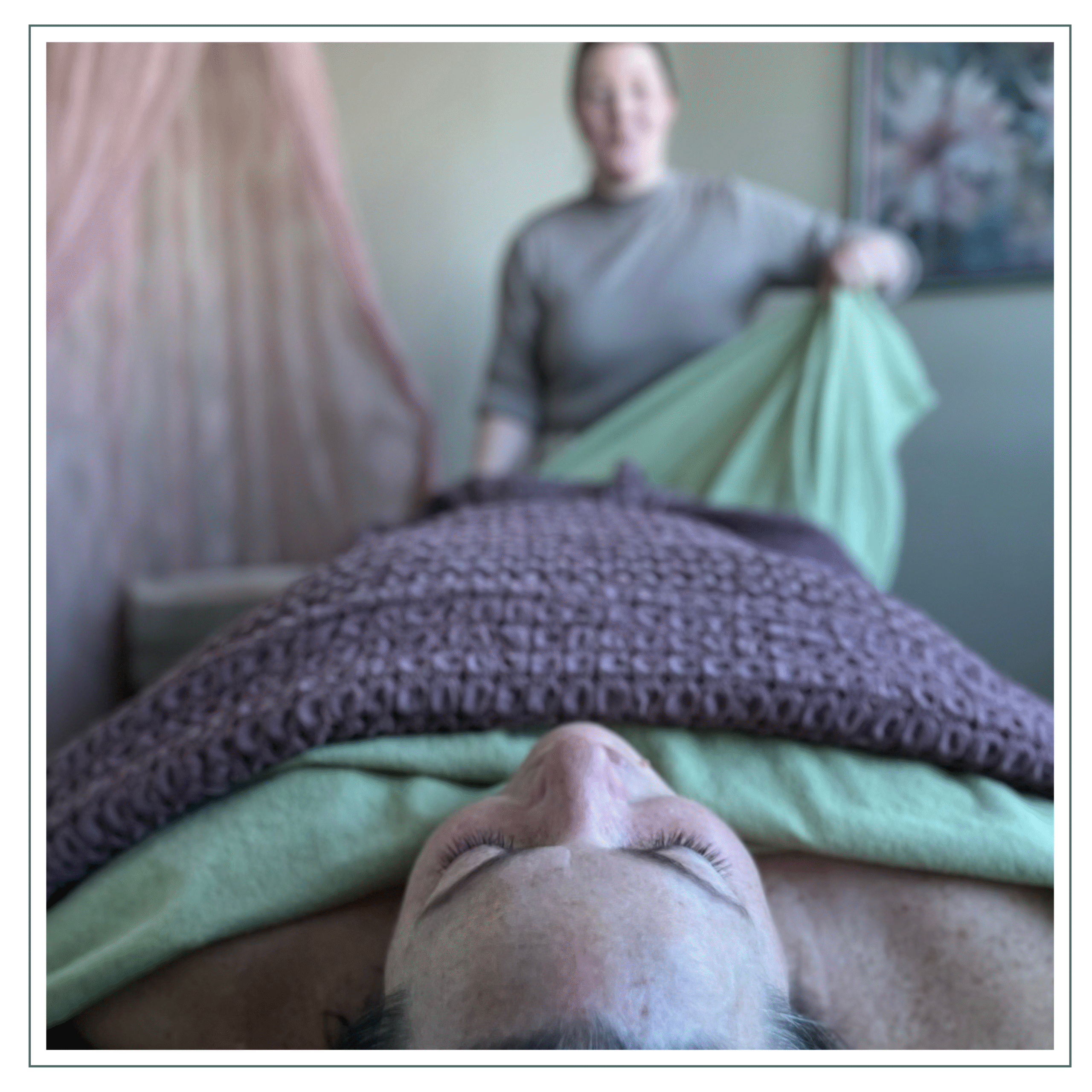 A person is receiving a massage while being covered with blankets. The massage therapist is adjusting the sheets in the background.